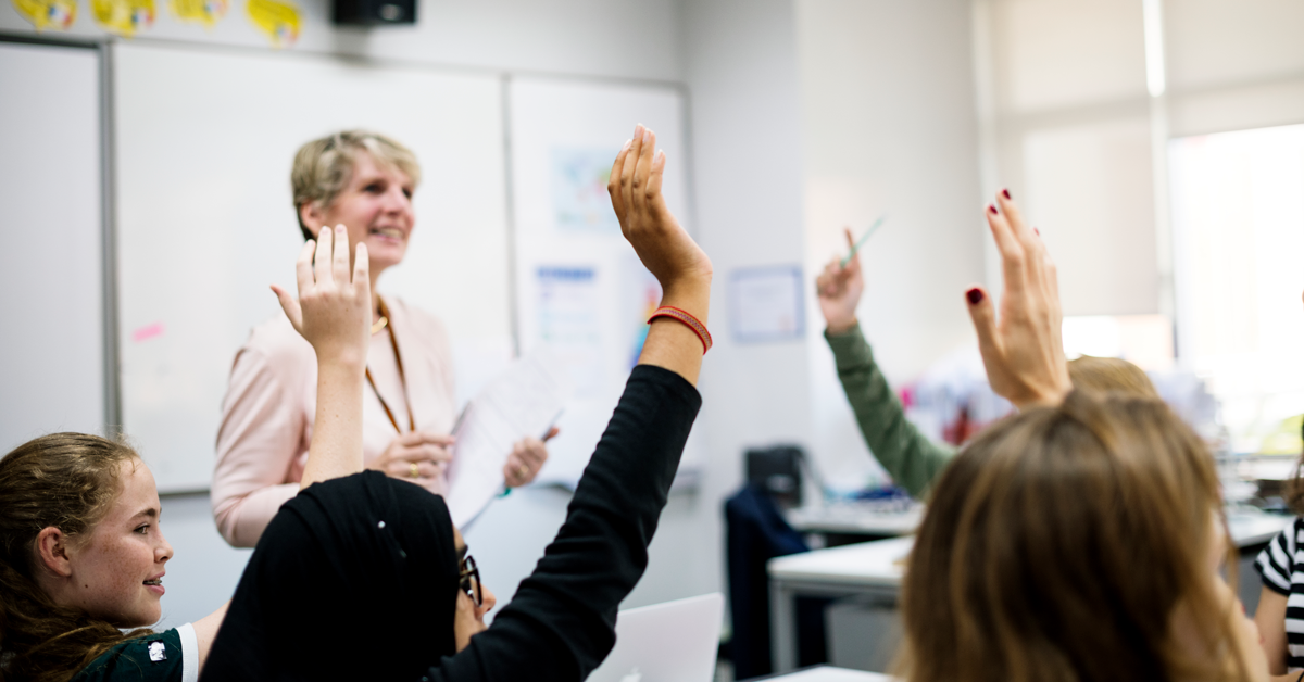 Teacher looking at several raised hands in the classroom.