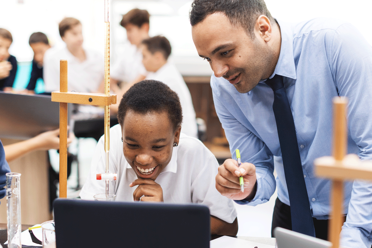 Teacher and student looking at laptop together and smiling.
