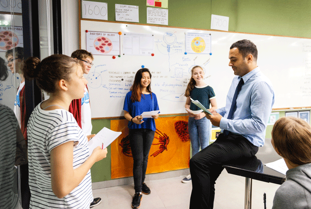 Teacher talking with teen students in classroom setting.