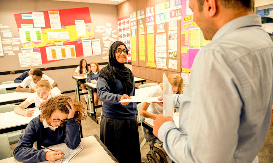 smiling student handing a worksheet to her teacher